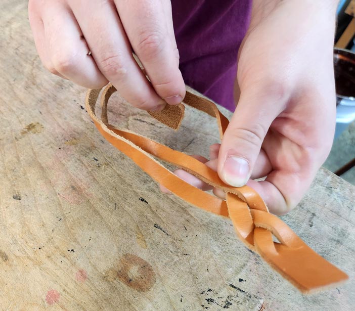 Putting end through leftmost slot of leather bracelet.